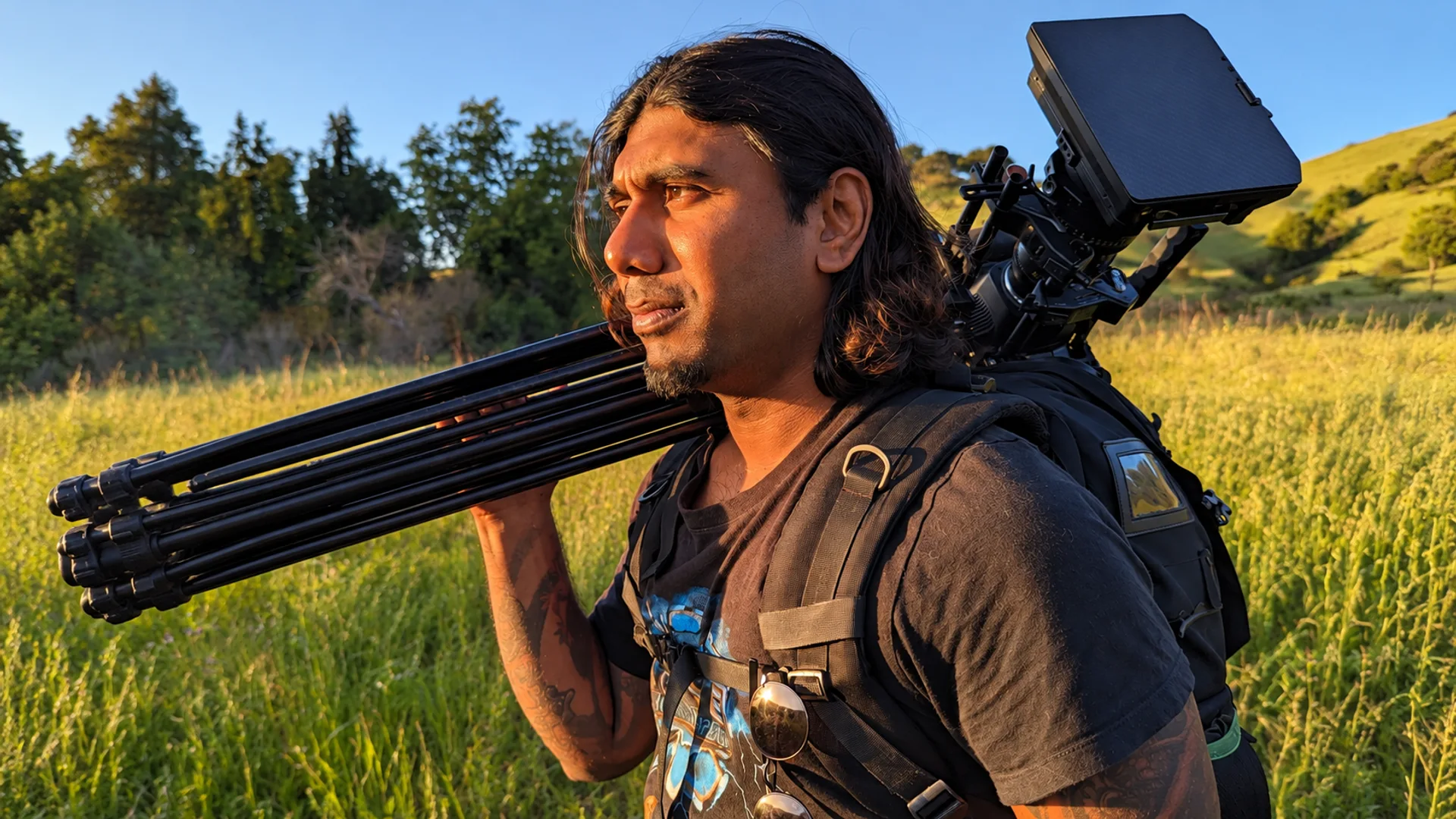 Neil carrying his cinema camera and tripod on a trail in the evening light